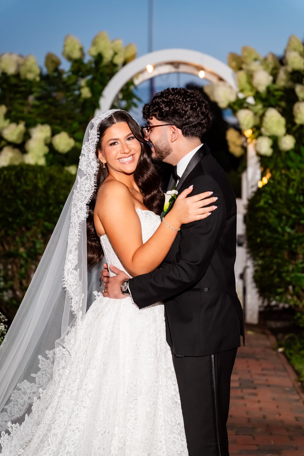 Bride smiling with her groom under a floral arch